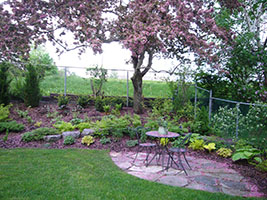 small paved patio in front of a shrub border and a pink crabapple in bloom